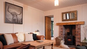 A cozy living room with a brown leather sofa, a wooden coffee table, a fireplace, and a framed picture on the wall. - Cosy and stylish, dog and family friendly cottage just south of Aviemore (Dalraddy)