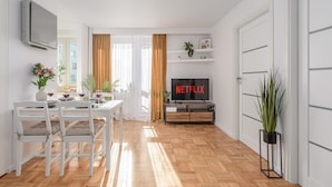 A modern living room with a dining area, a flat-screen TV, and a potted plant. - Lumina apart with balcony in Warsaw (Warsaw)