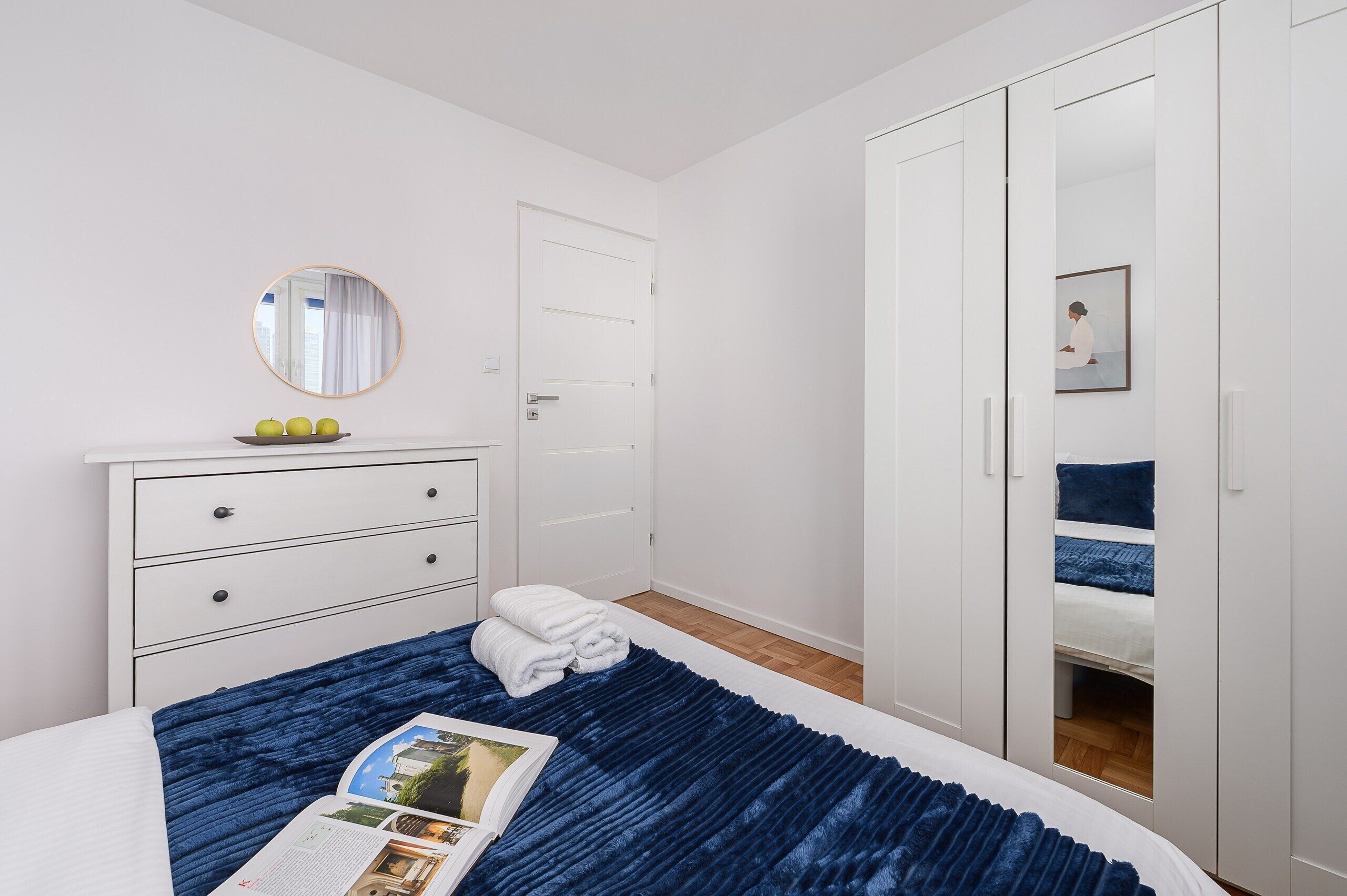 Une chambre à coucher avec un lit, une commode, un miroir, une armoire et une fenêtre.