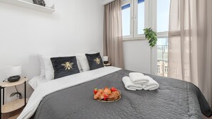 A neatly made bed with a dark quilt, a basket of croissants and strawberries, and a window with curtains. - Lumina apart with balcony in Warsaw (Warsaw)