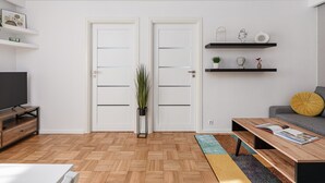 A modern living room with a wooden floor, a TV stand, a sofa, a coffee table, and a bookshelf. - Lumina apart with balcony in Warsaw (Warsaw)