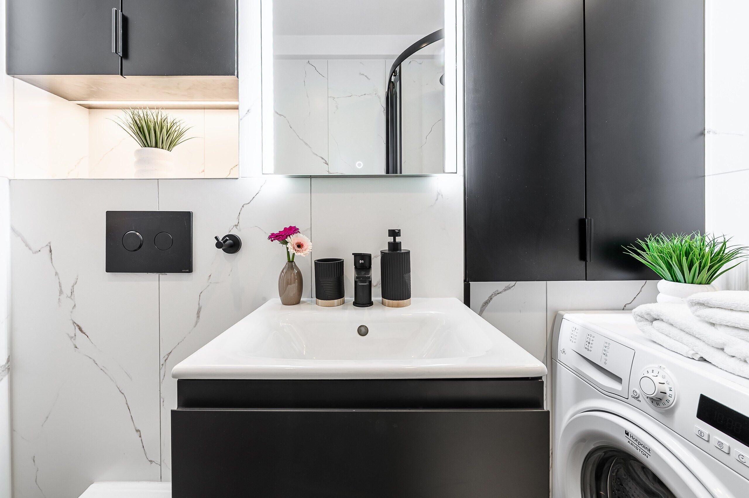 Un bagno moderno con un lavandino bianco, mobili neri, uno specchio, una doccia e una lavatrice.