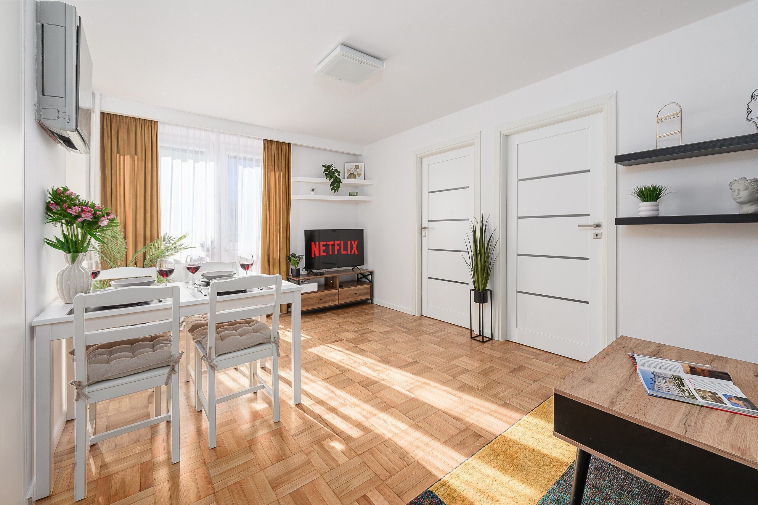 A modern living room with a dining area, a flat-screen TV, and a bookshelf.