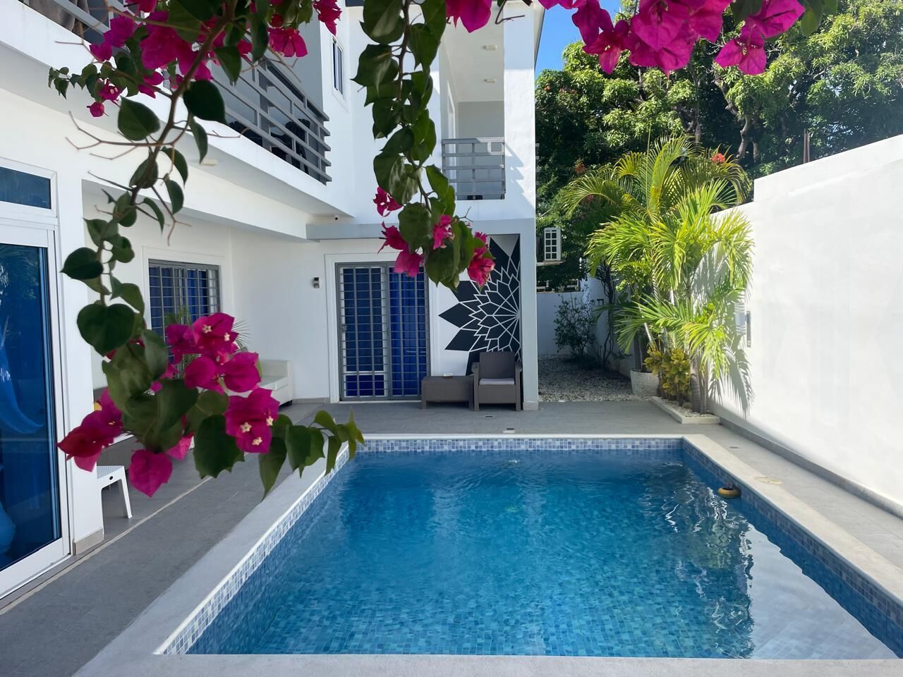 A swimming pool with a clear blue water, surrounded by a white building with a balcony and a door.