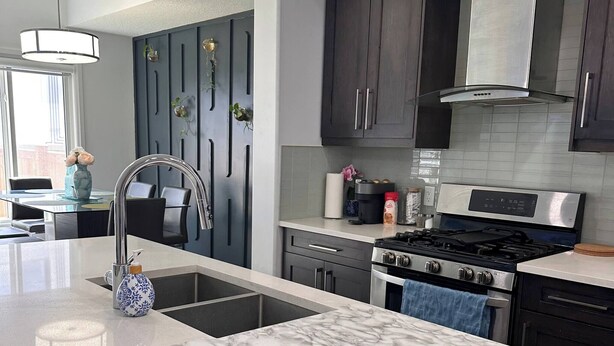 A modern kitchen with dark cabinetry, a large island with a marble countertop, stainless steel appliances, and a pendant light. - Modern 3BR Home Edmonton Near by Airport (Edmonton)