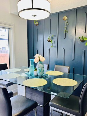 A modern dining area with a glass table, black chairs, and a blue accent wall with vertical lines. - Modern 3BR Home Edmonton Near by Airport (Edmonton)