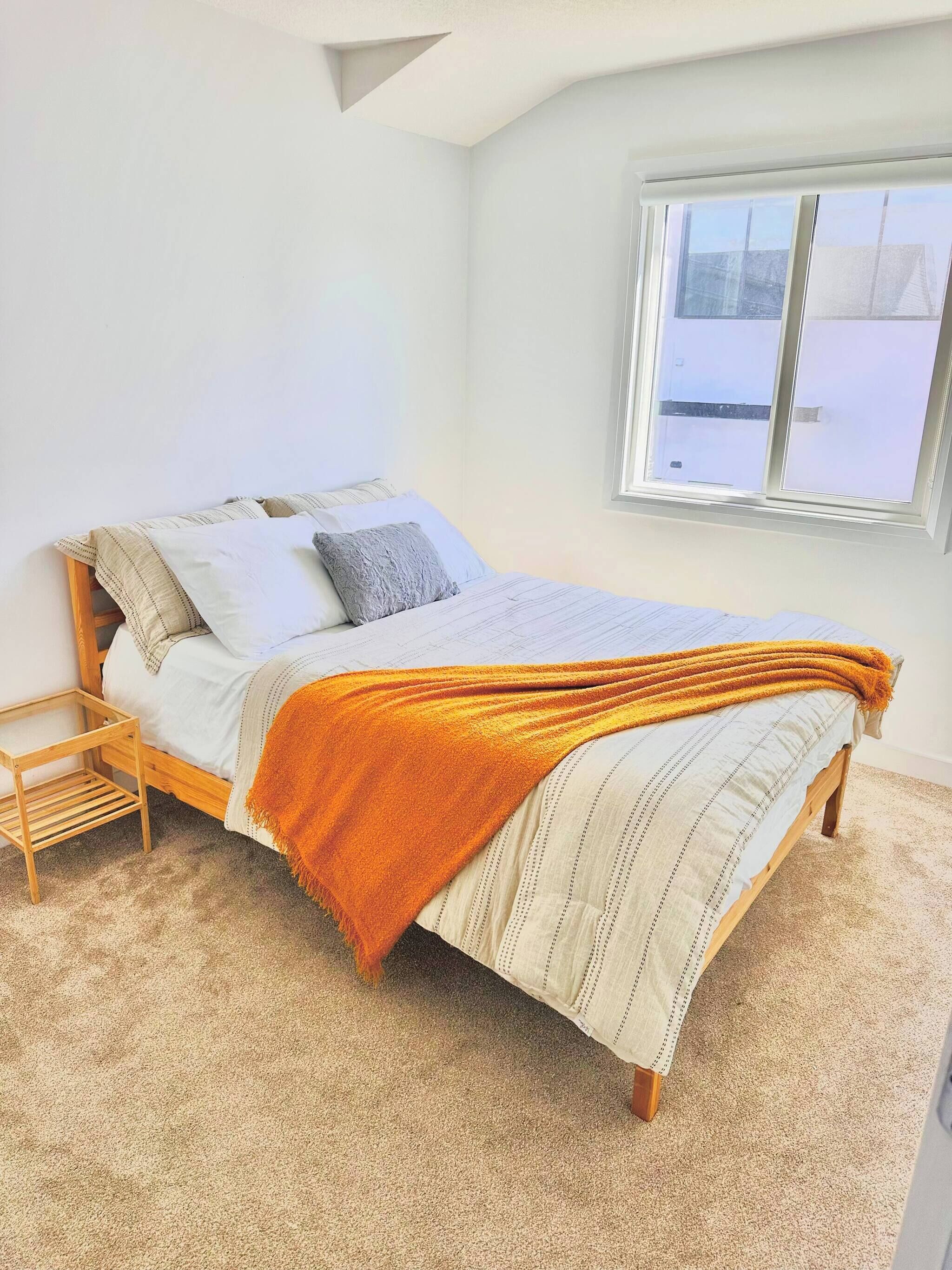 Une chambre à coucher avec un lit, une fenêtre et une petite table de chevet en bois.
