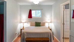Ein Schlafzimmer mit einem Bett, Nachttischlampen, einem Fenster, einer Bank und einer Tür.