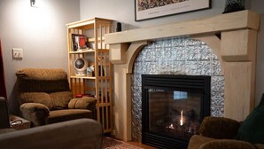 Ein gemütliches Wohnzimmer mit Kamin, Holzregal und einem gemusterten Teppich.