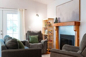 A living room with a fireplace, a bookshelf, and a window with curtains. - ‘Cedar’ Riverfront Cabin near Olympic National Park (Beaver)