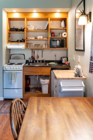 A compact kitchen with a stove, sink, and wooden shelves above.