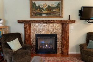 A living room with a fireplace, two armchairs, a television, and a painting on the wall. - ‘Hemlock’ Riverfront Cabin near Olympic National Park (Beaver)