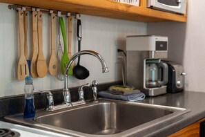 A kitchen with a stainless steel sink, wooden utensils hanging on the wall, and a coffee maker on the countertop. - ‘Hemlock’ Riverfront Cabin near Olympic National Park (Beaver)