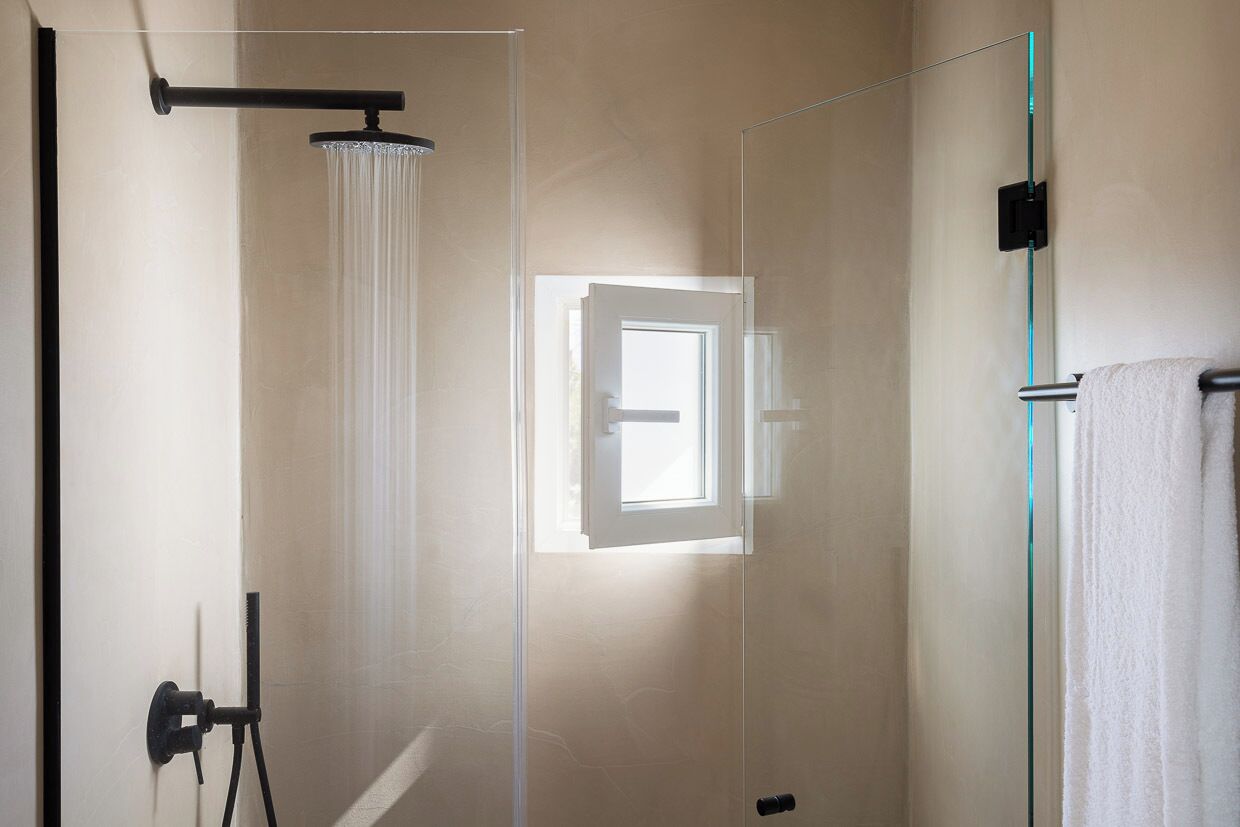 Un baño moderno con cabina de ducha de vidrio, toallero a la vista y puerta con ventanal.