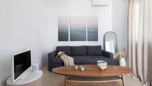 Ein modernes Wohnzimmer mit einem Flachbildfernseher, einem dunkelgrauen Sofa, einem Holztisch und einem großen abstrakten Gemälde über dem Sofa.