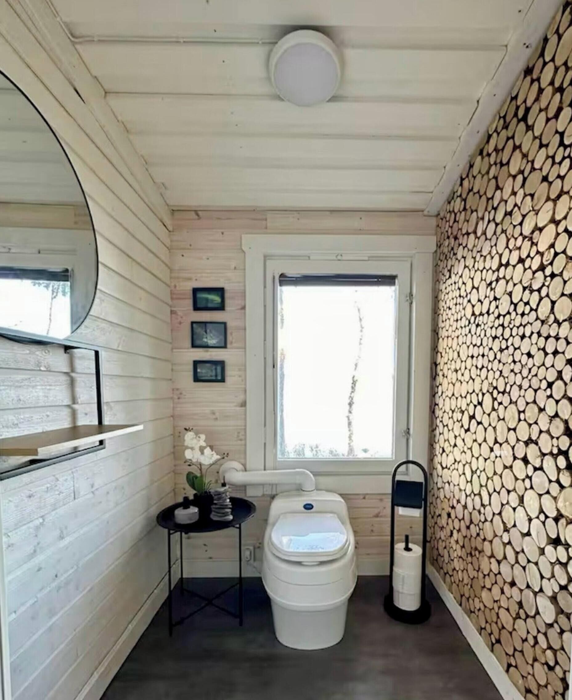 A compact bathroom with a toilet, a small table with a plant, and a window.