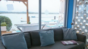 A gray sofa with blue cushions and a striped throw blanket in a room with large windows overlooking a body of water. - Wax Hostel & Apts (Faro)