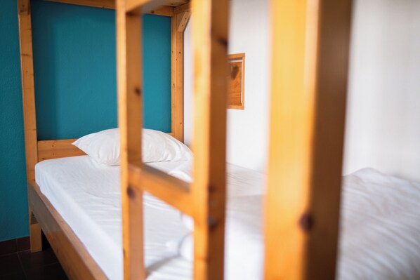A bunk bed with white bedding, wooden frame, and a teal wall. - Wax Hostel & Apts (Faro)