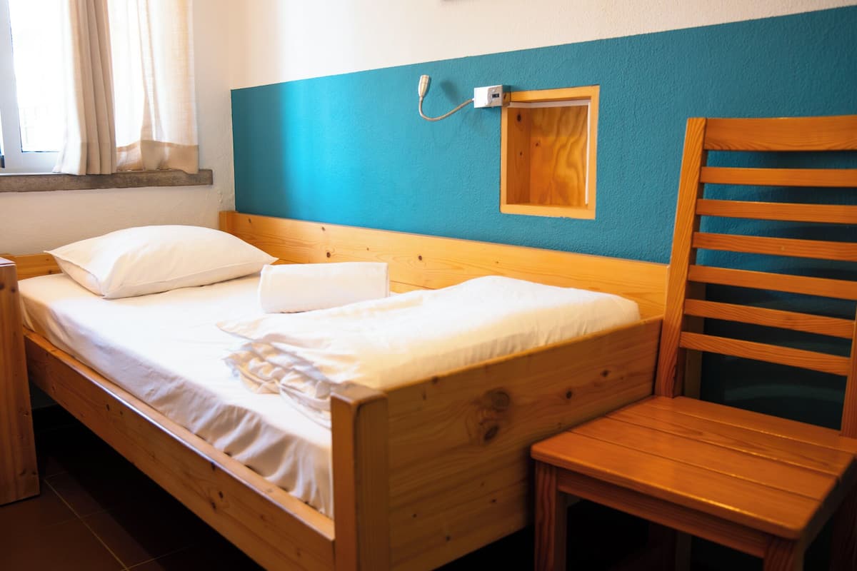 A wooden bed with a headboard, a wooden chair, and a small wooden cabinet against a teal wall.