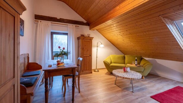 Un accogliente sottotetto con soffitto in legno, un tavolo da pranzo con sedie, un divano verde e un piccolo tavolino rotondo.
