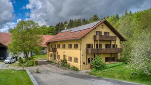 Un edificio giallo di due piani con tetto in tegole rosse, balconi in legno e vialetto lastricato.