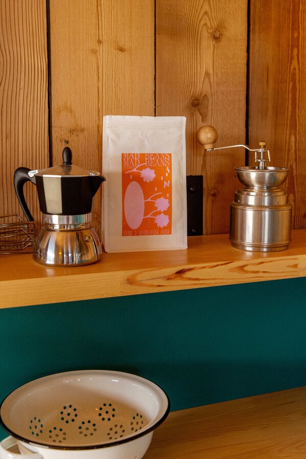Una encimera de cocina con una cafetera, un saco de granos de café, un molinillo y un colador.