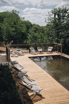 Una terraza de madera con sillones de descanso y una piscina.