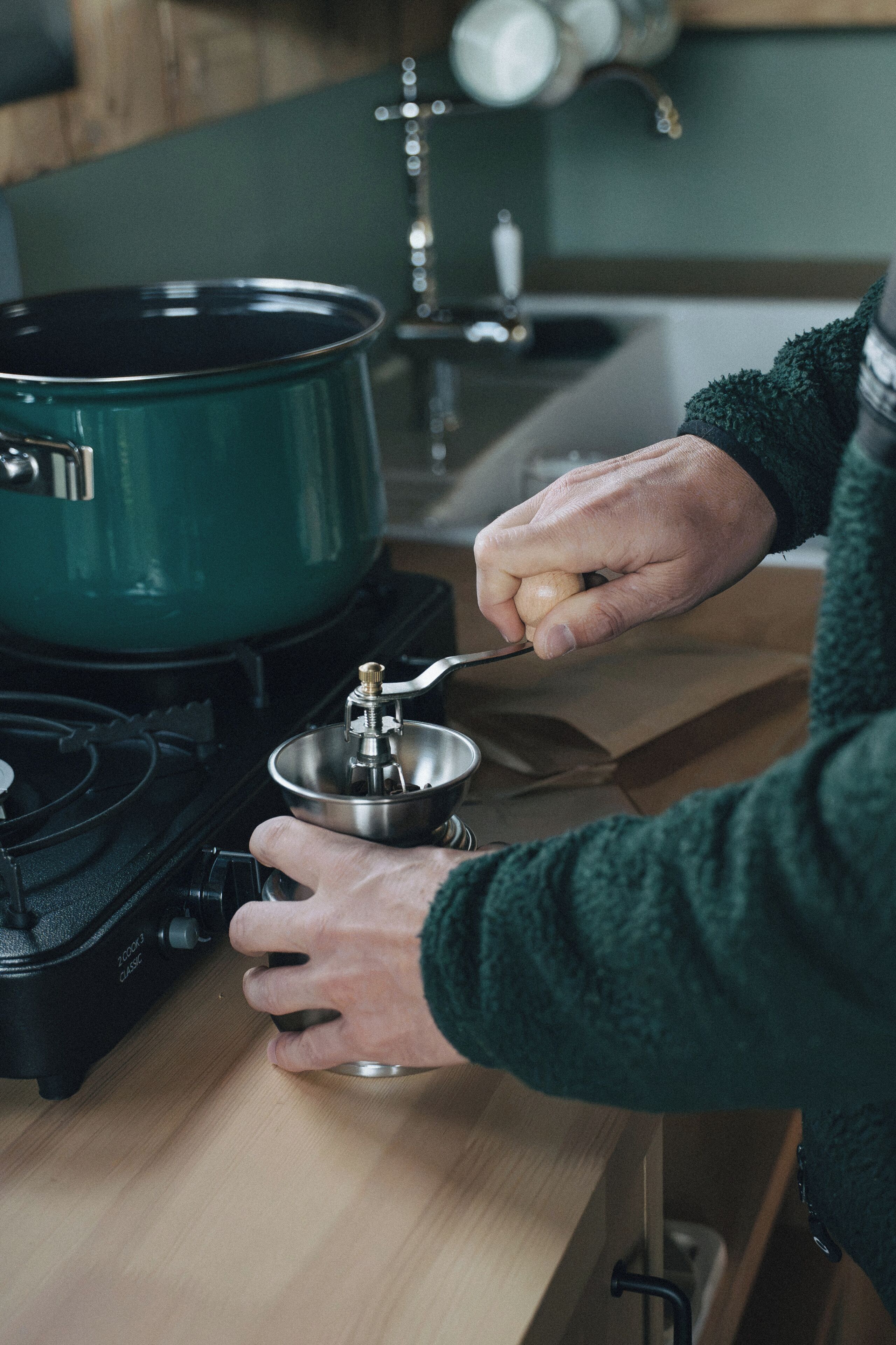 A person cooking with a green pot on a stove.