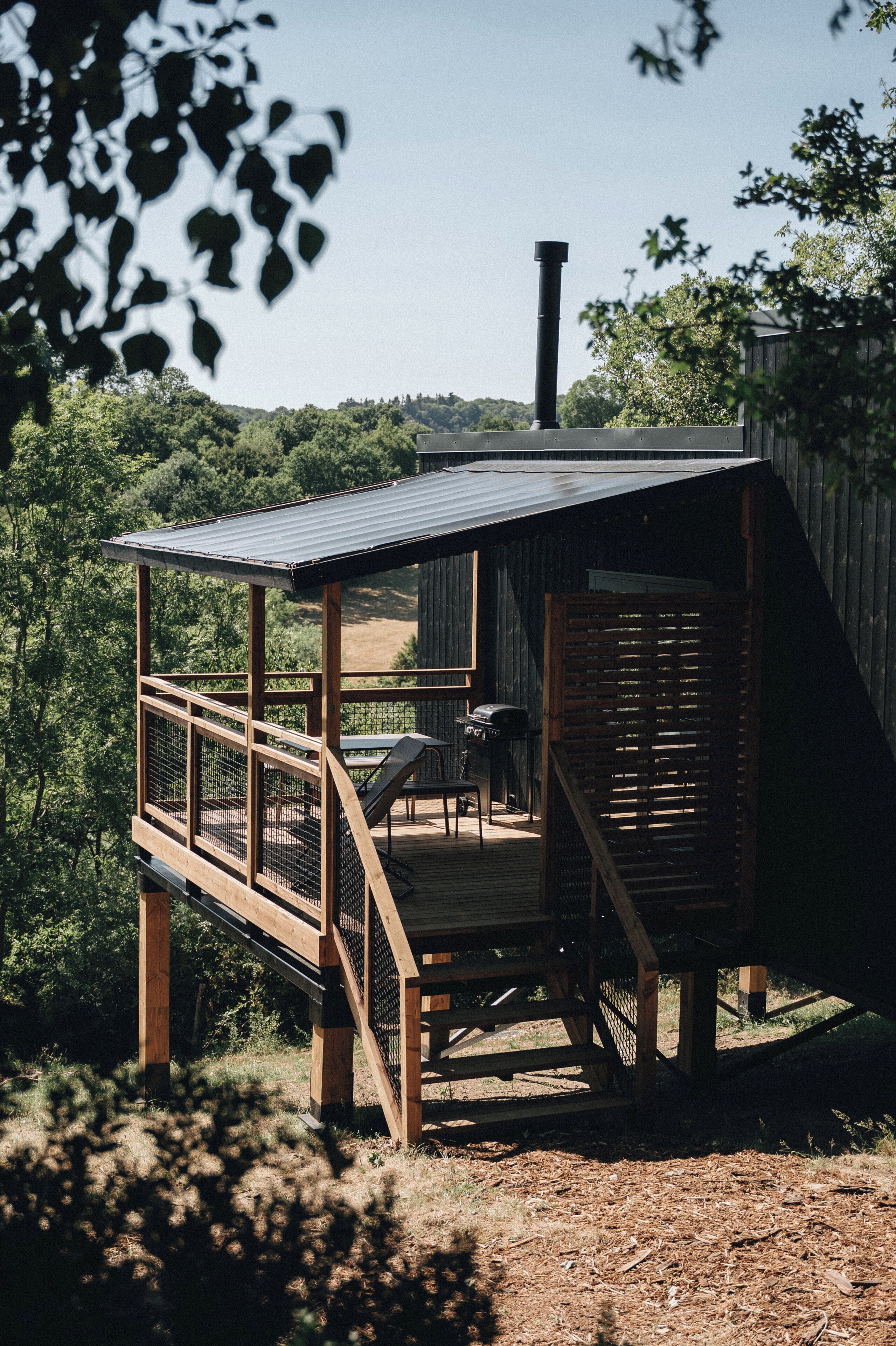 Una terraza de madera con techo metálico, rodeada de árboles y vista a zona boscosa.