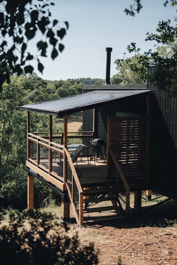 A wooden deck with a metal roof, surrounded by trees and a view of a forested area.