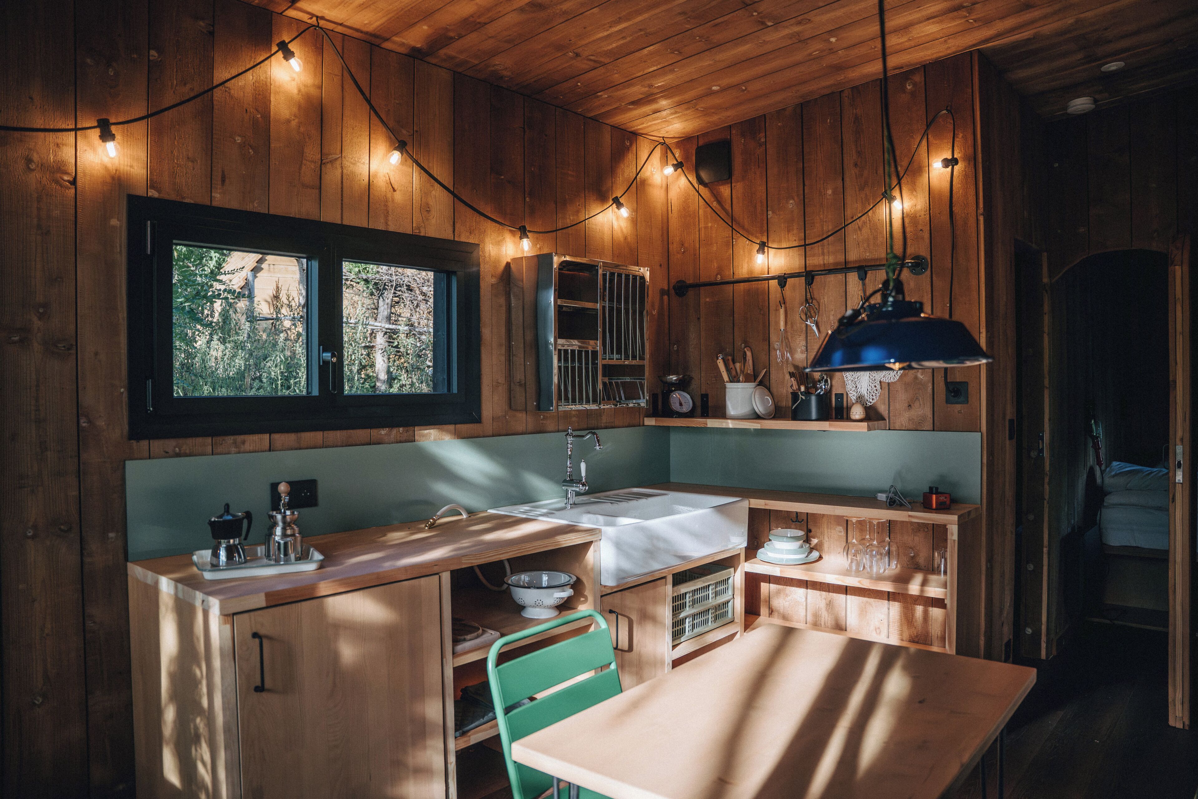 Cocina compacta con paredes de madera, una ventana, un lavabo, una estufa y una zona de comedor con mesa y sillas.