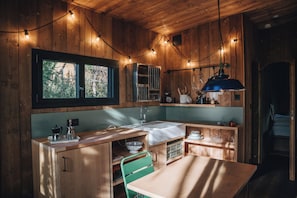 Cocina compacta con paredes de madera, una ventana, un lavabo, una estufa y una zona de comedor con mesa y sillas.