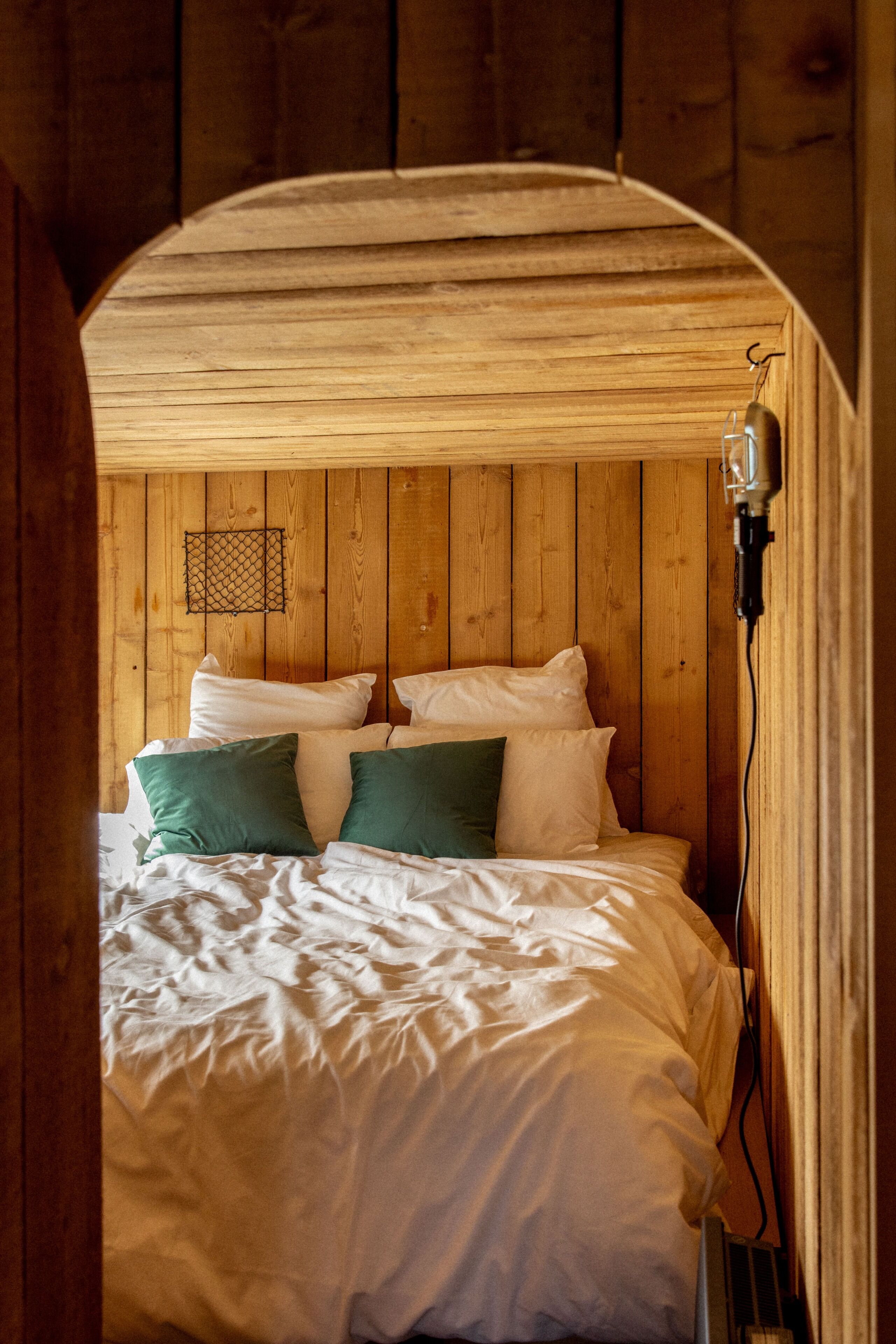 Un dormitorio tipo cabaña de madera con una cama, almohadas y una lámpara colgante.