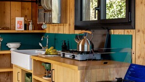 A wooden interior with a kitchen area, including a stove, kettle, and a window with a view of greenery. - Bon Air club Alpes Mancelles (Saint-Léonard-des-Bois)