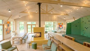 A spacious indoor area with a fireplace, climbing wall, and multiple seating arrangements. - Bon Air club Alpes Mancelles (Saint-Léonard-des-Bois)
