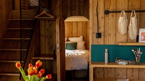 A wooden interior with a bed, a hanging light, a shelf with kitchen utensils, and a staircase. - Bon Air club Alpes Mancelles (Saint-Léonard-des-Bois)