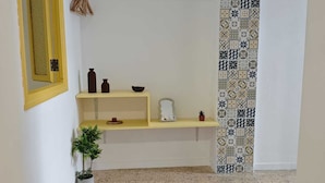 Una habitación con pared estampada, un espejo con marco amarillo, una planta pequeña y una alfombra tejida.