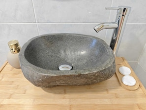 A stone sink with a modern faucet, a soap dispenser, and two soap bars on a wooden tray.