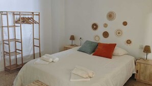Un dormitorio con una cama, un banco de madera, una lámpara colgante, un armario de madera y decoración en la pared.