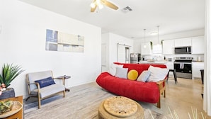 A modern living room with a red sofa, a grey armchair, and a ceiling fan. - Unit 101 Family-friendly stay San Antonio 2BR for 6 (San Antonio)