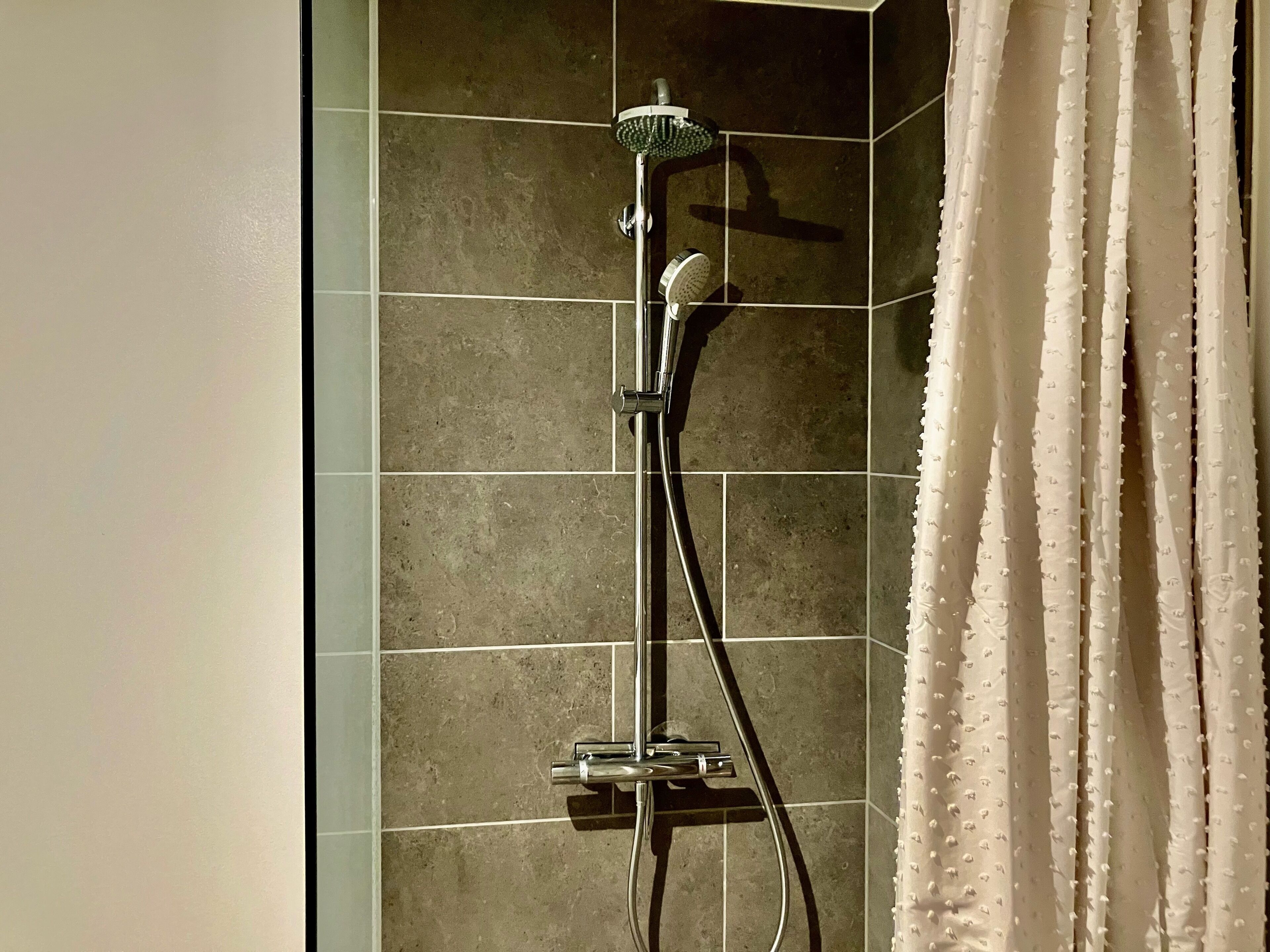 A shower with a handheld showerhead and a wall-mounted control.