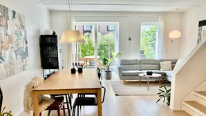 Moderni olohuone, jossa on puinen ruokapöytä, harmaa sohva ja portaat.