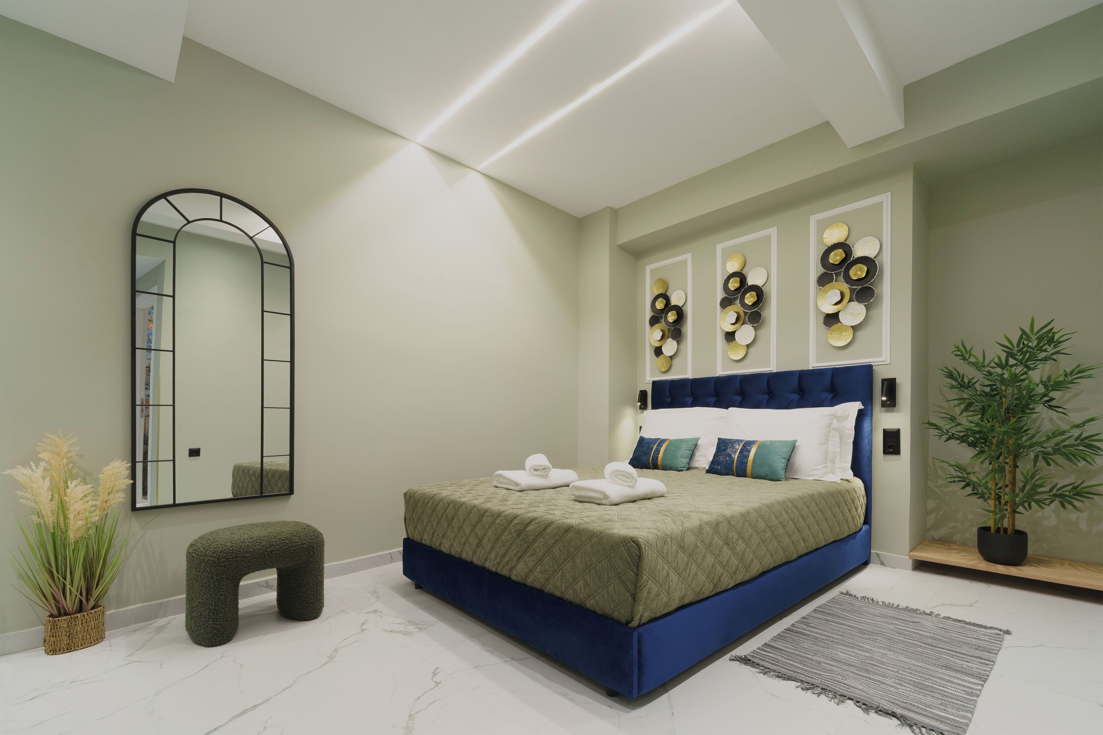 A modern bedroom with a bed, a bench, a mirror, wall art, and a potted plant.