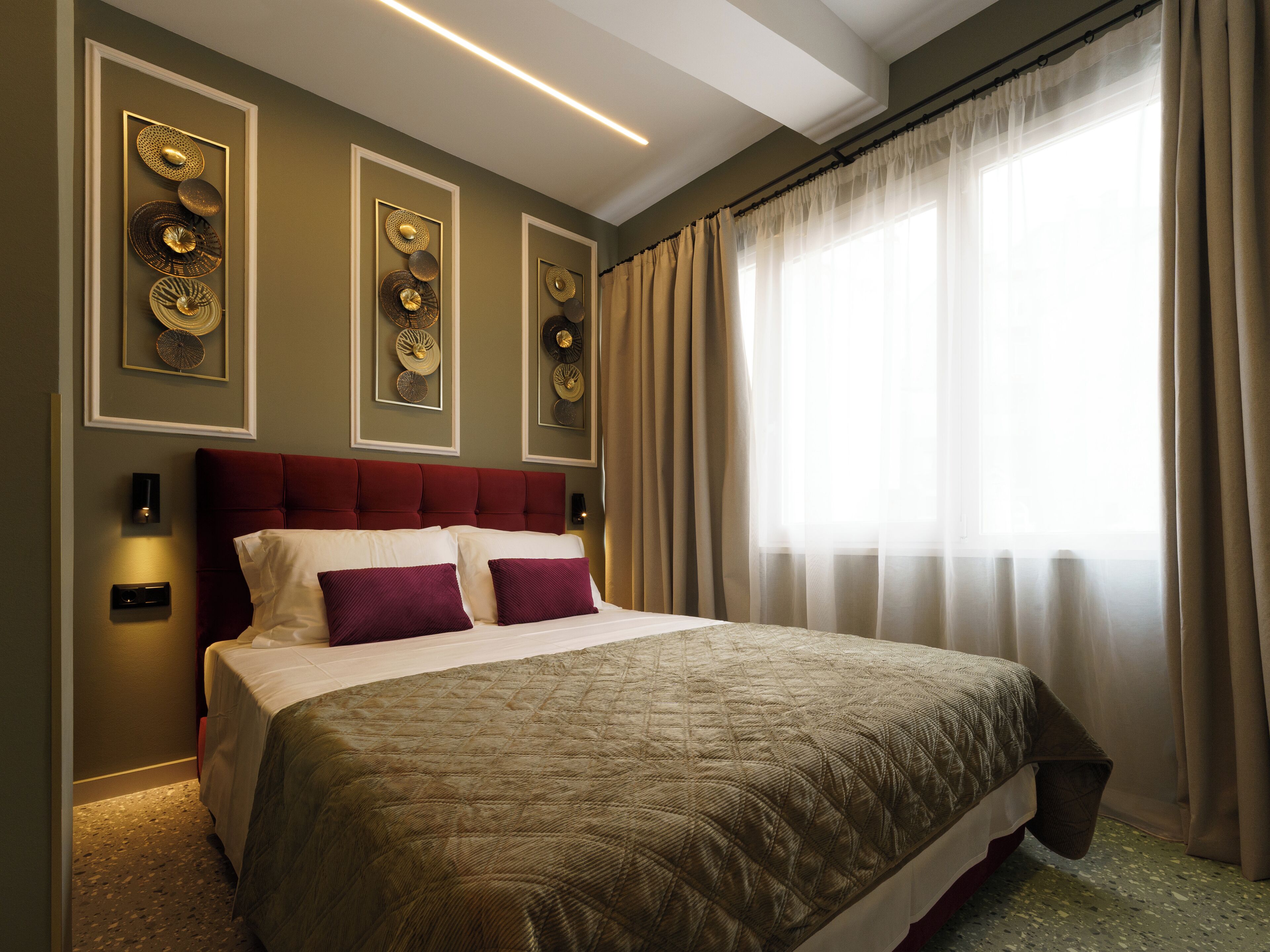 A hotel room with a large bed, a red headboard, wall sconces, and a window with curtains.