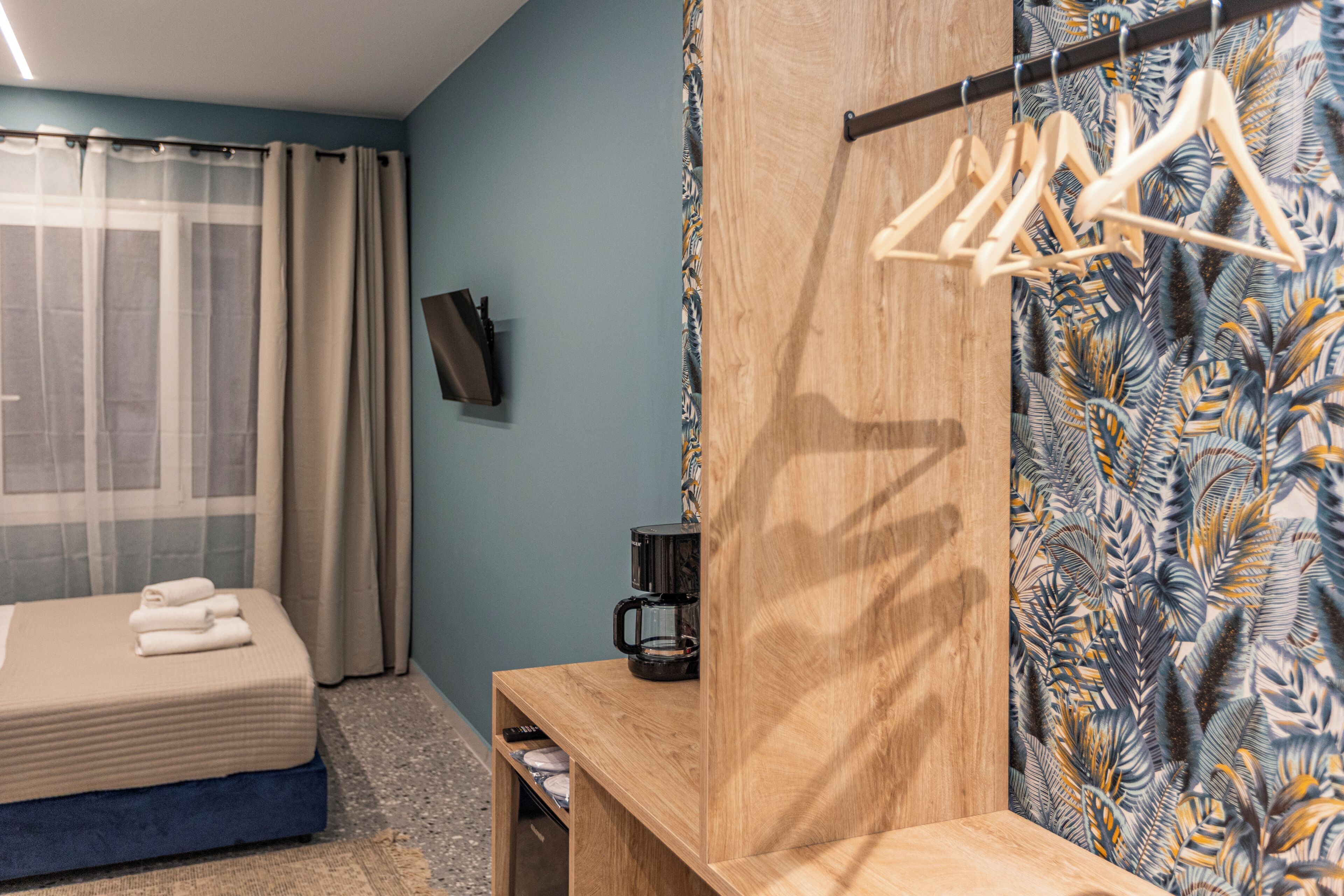 A bedroom with a bed, a wooden bench, a coffee maker, and a wall-mounted TV.