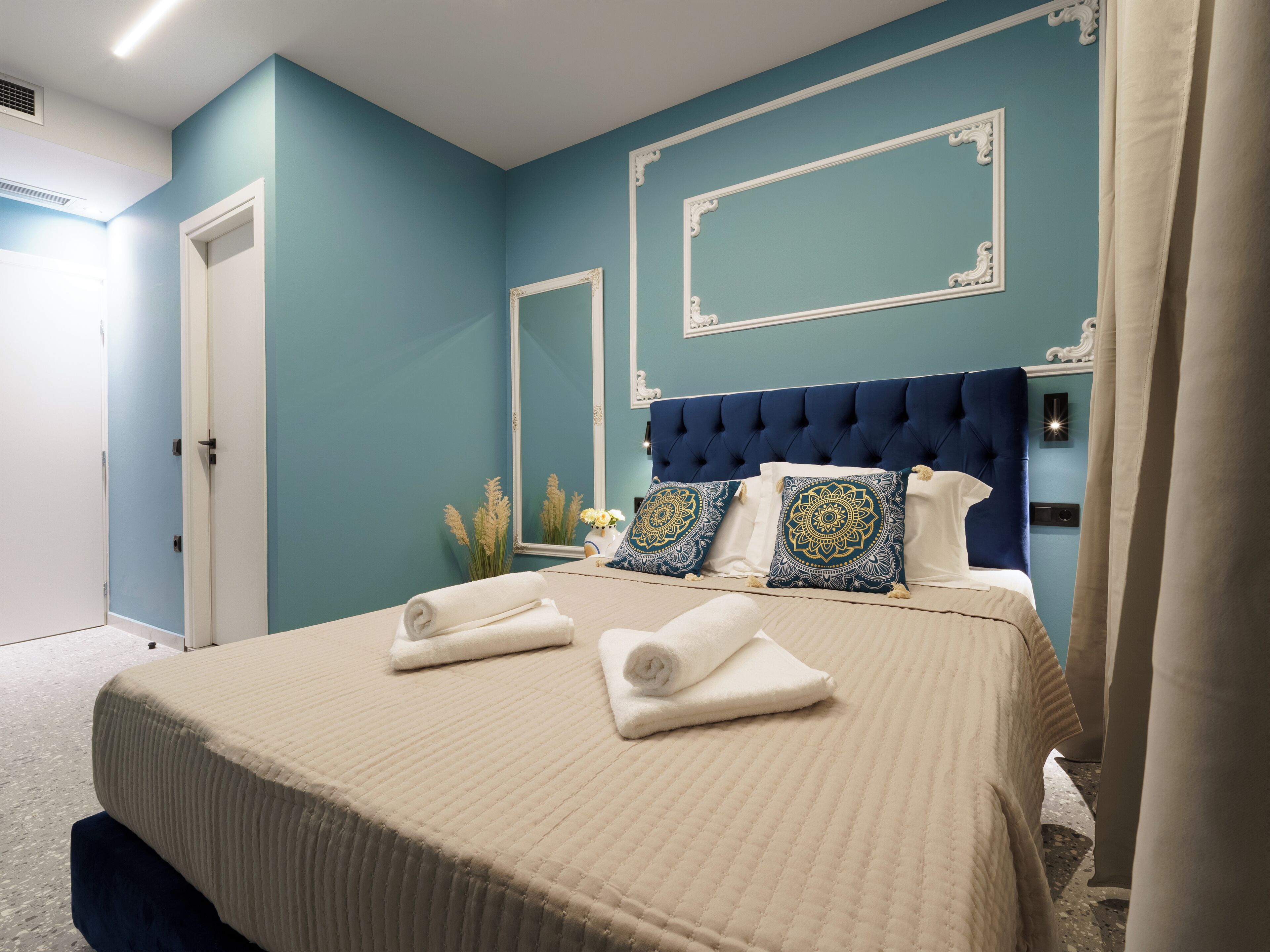 A bedroom with a blue wall, a tufted headboard, and a bed with white and patterned pillows.
