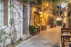 A narrow street with outdoor seating, a building with a yellow door, and a sign with a person riding a bicycle. - Ernest Suites Psiri (Athens)