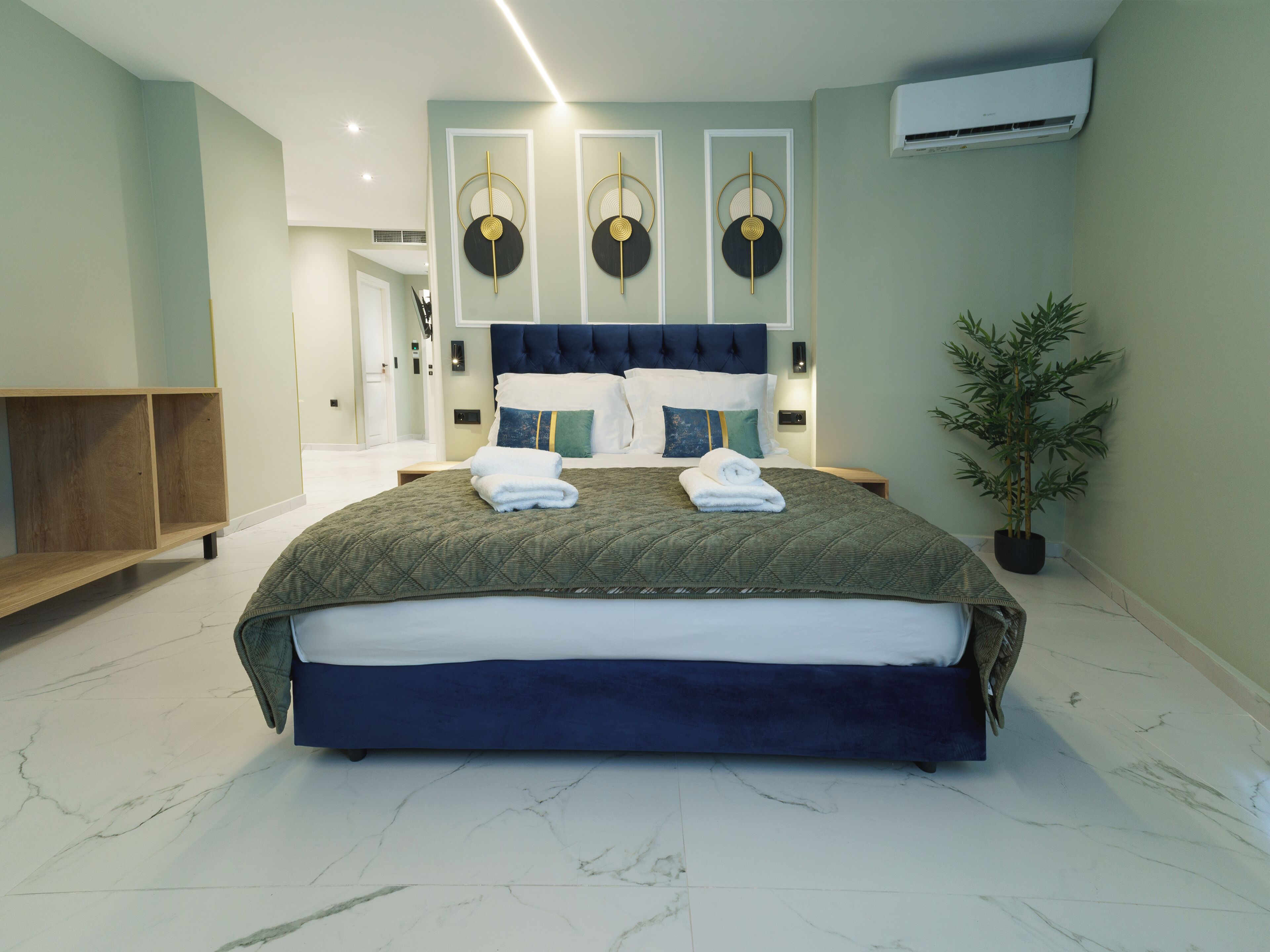 A modern bedroom with a large bed, a headboard, a bedside table, a potted plant, and a wall-mounted air conditioner.