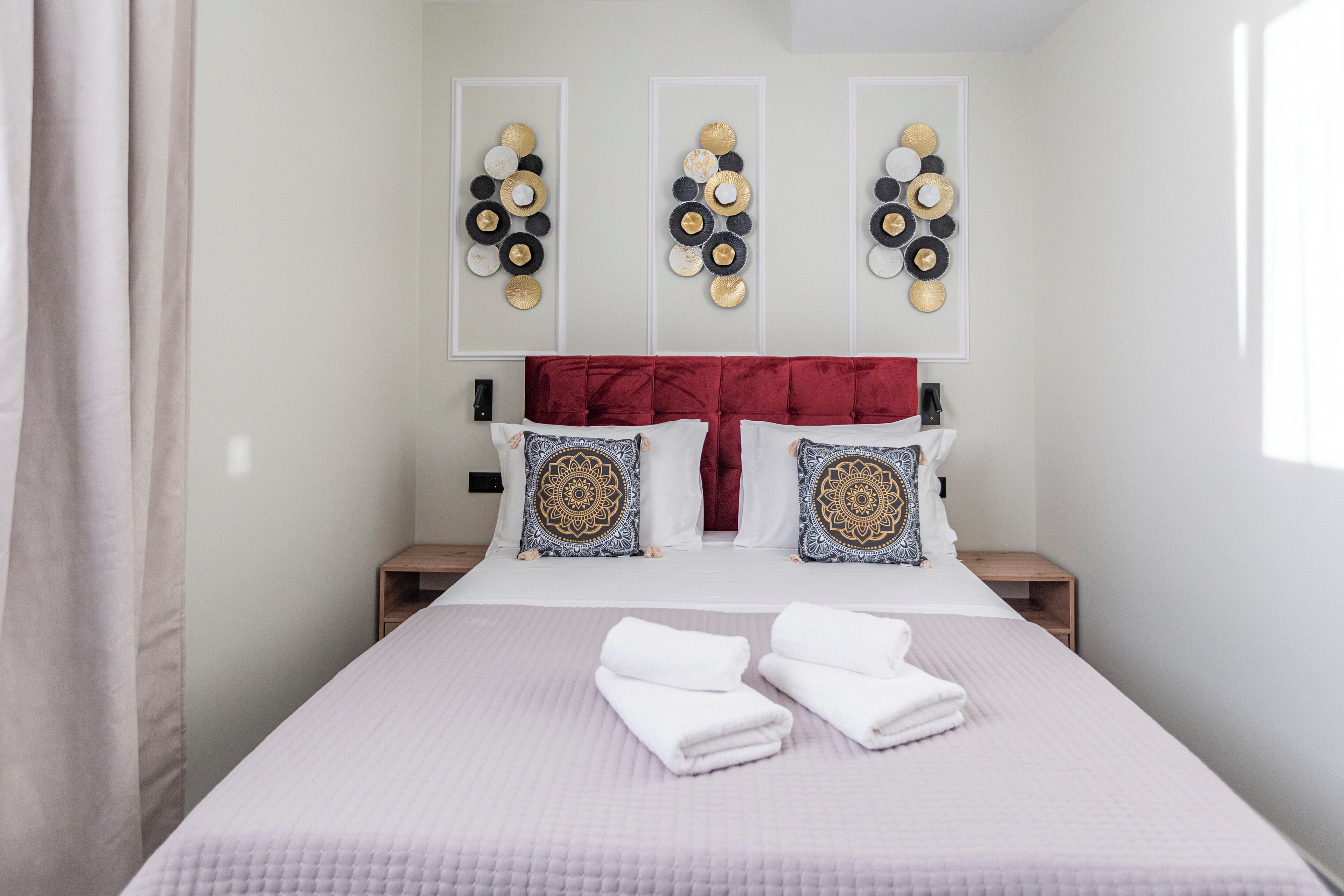 A neatly made bed with pillows, a red headboard, and wall art.
