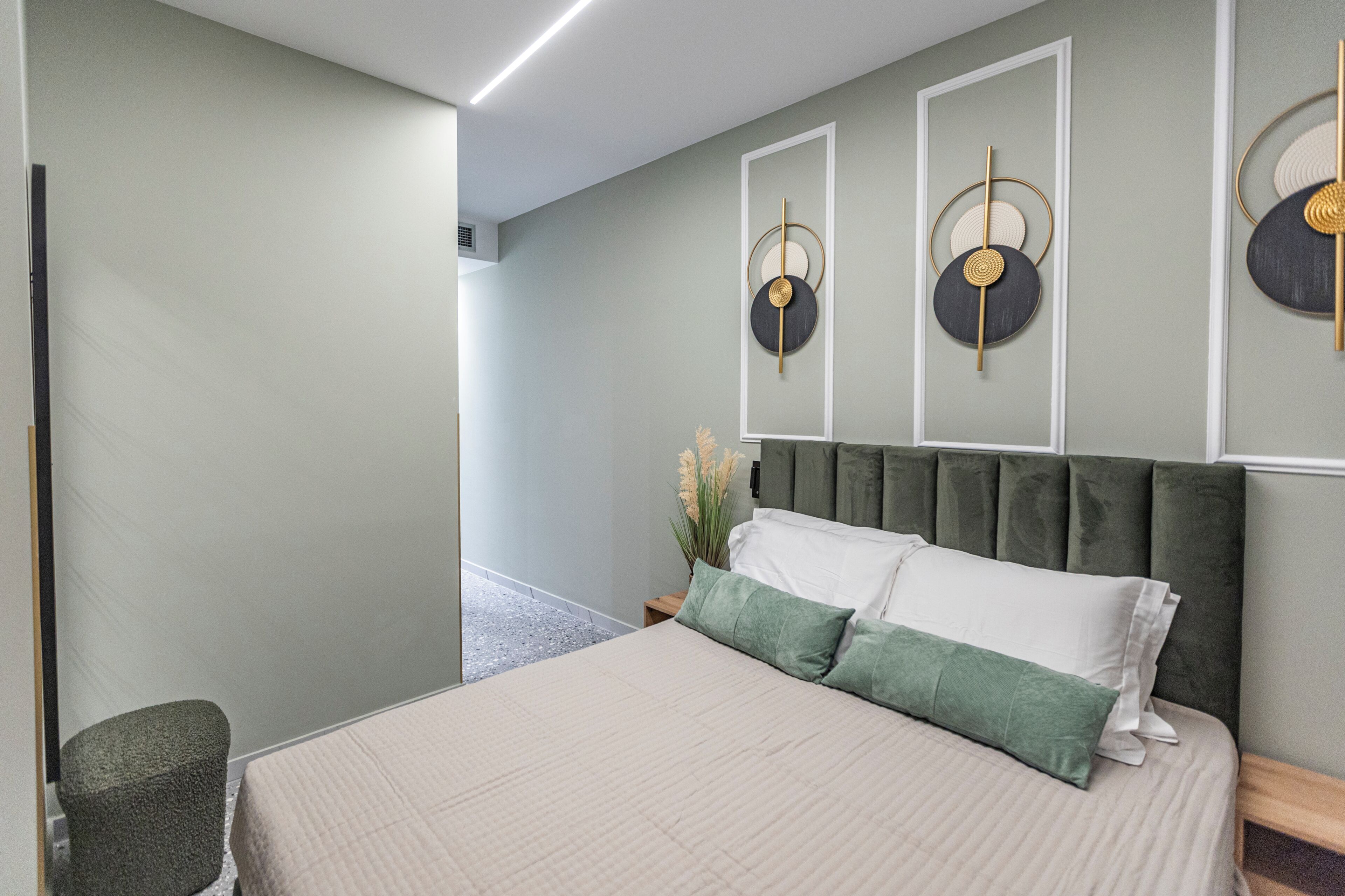 A modern bedroom with a large bed, a headboard, a bedside table, a chair, and wall art.